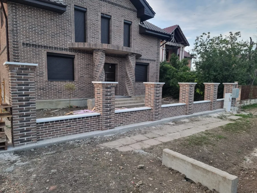 Casă din clincher închis cu balcon zidit și gard cu stâlpi din cărămidă